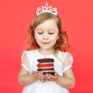 A little girl holding a cake with candles in it.