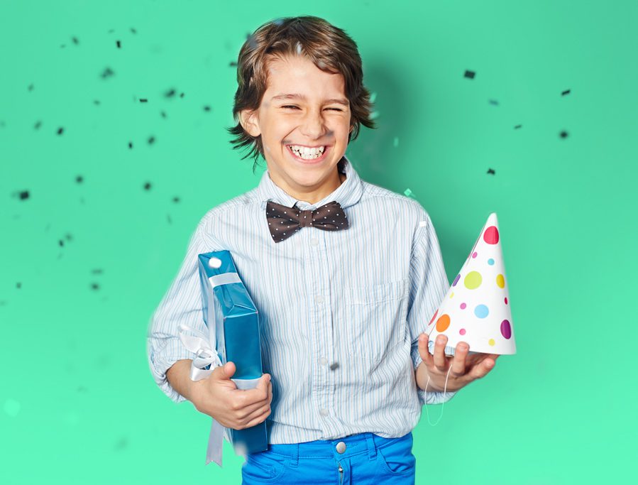 A boy holding a bottle and a party hat.