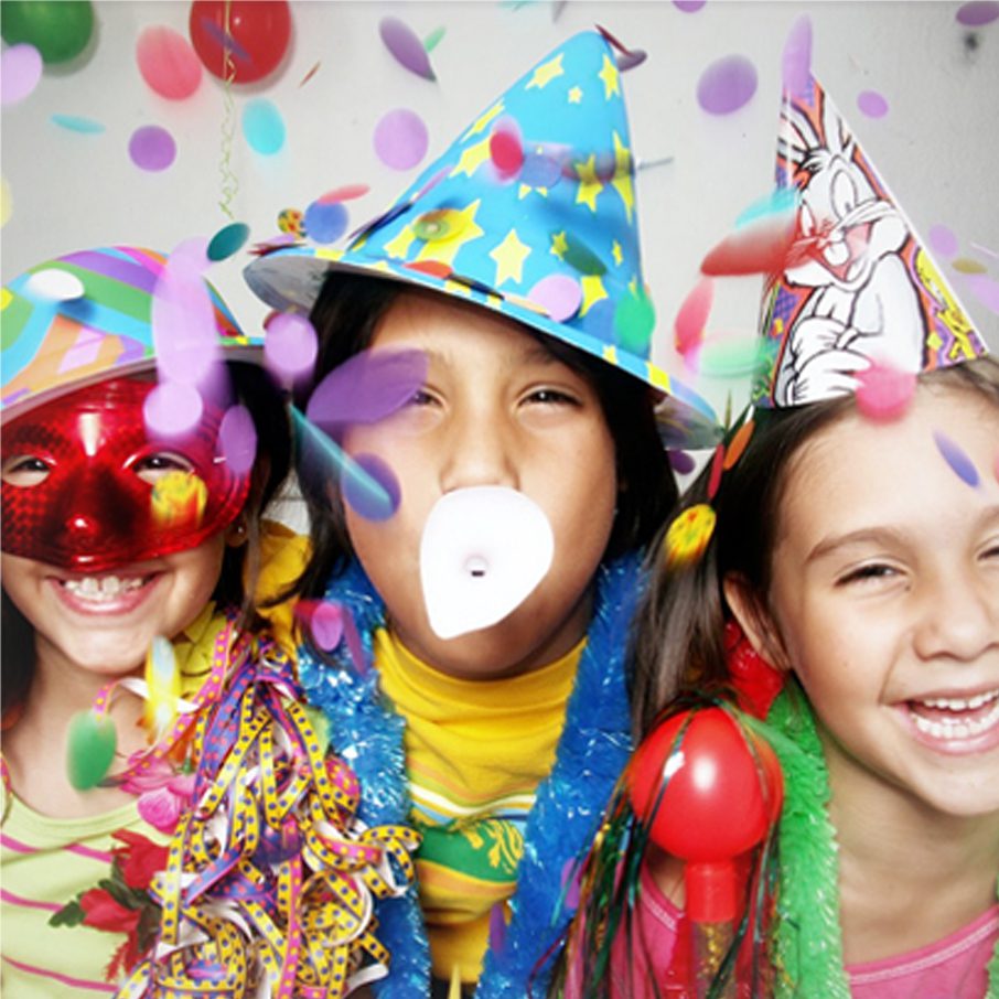 Three children wearing party hats and masks in a photo booth.