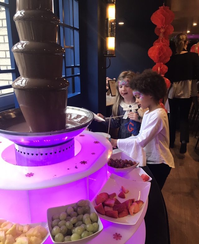 Two children are standing at a chocolate fountain.