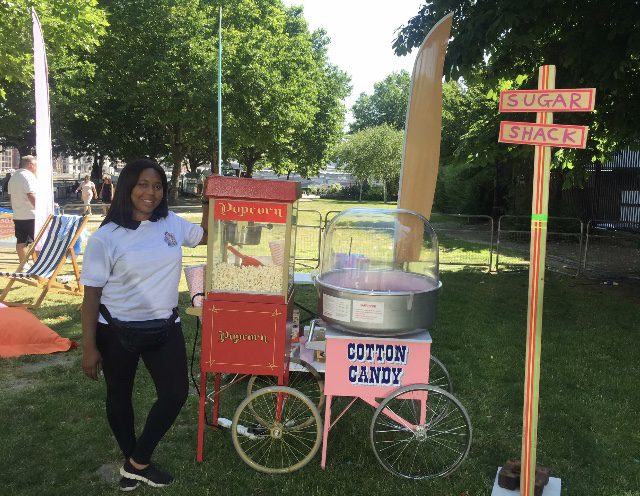 A woman standing next to an old fashioned cotton candy machine.