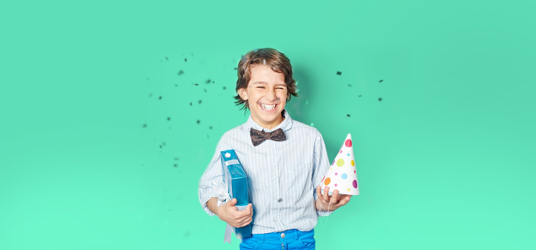 A boy holding a bottle and a party hat.