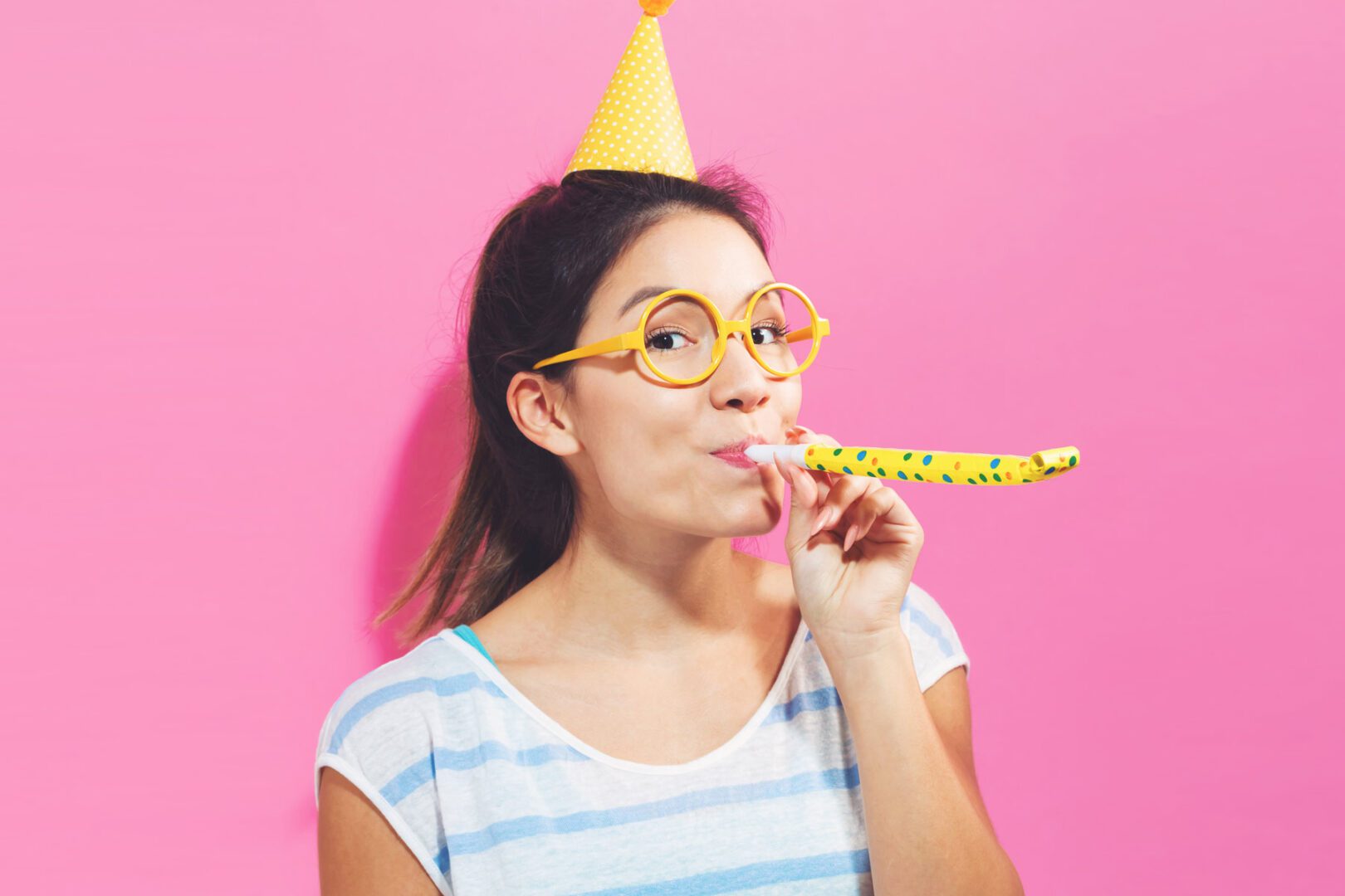 A woman wearing glasses and a party hat is eating some food.