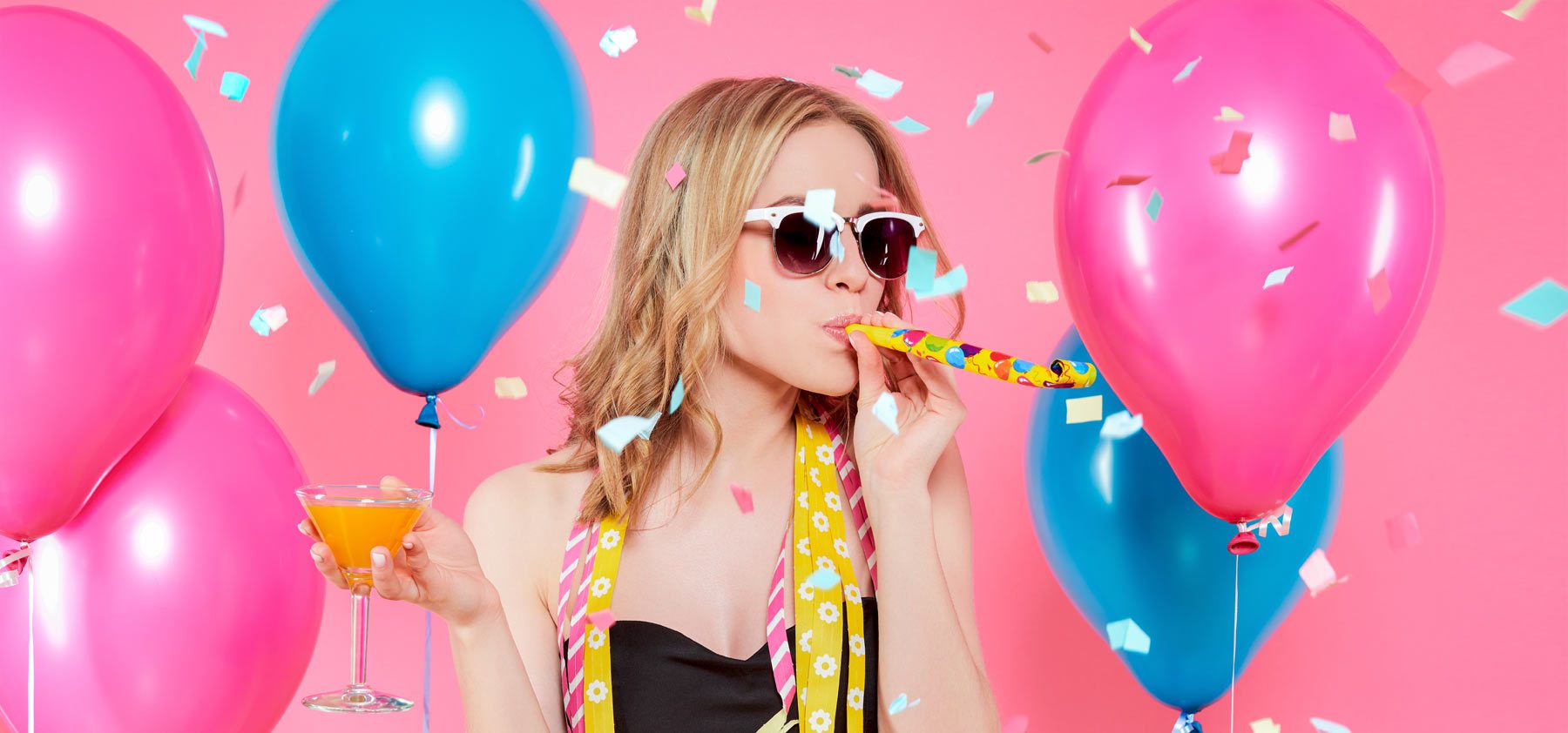 A woman with balloons and confetti blowing out of her mouth.