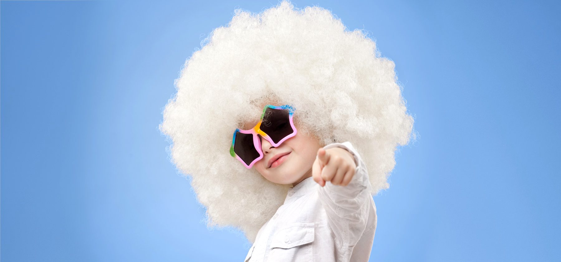 A child with a white wig and sunglasses pointing.