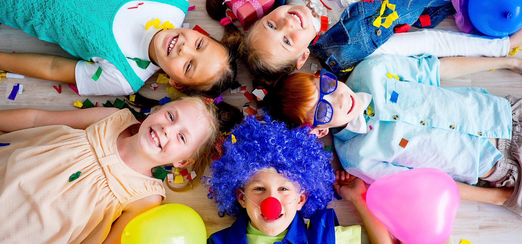 A group of children wearing clown wigs and holding balloons.