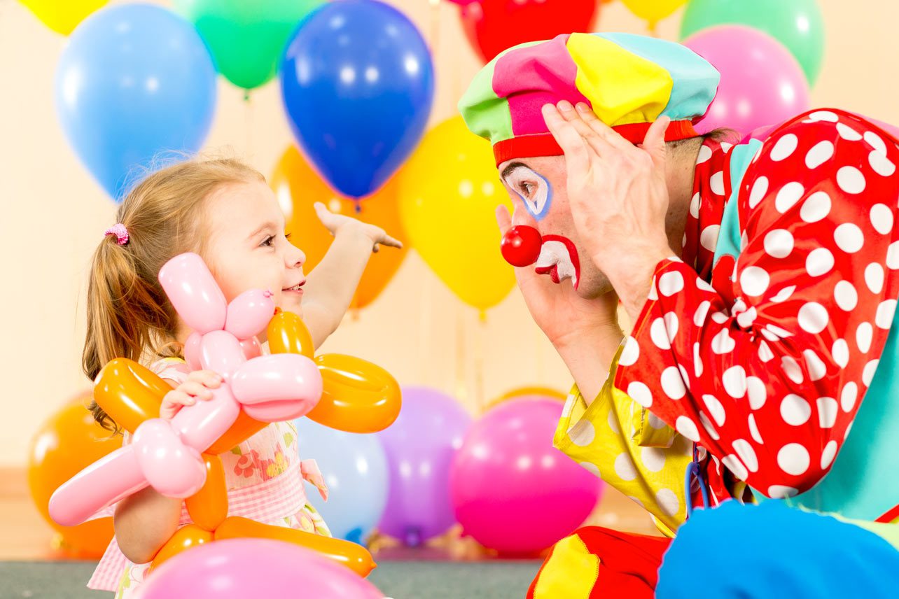 A clown and a little girl are playing with balloons.