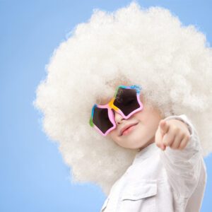 A child with white hair and sunglasses pointing at the camera.