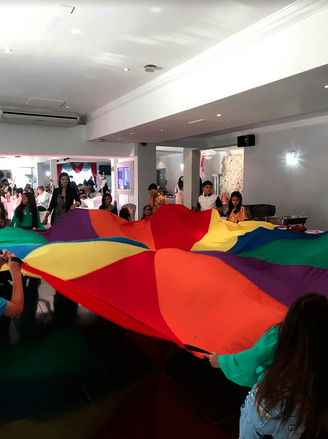 A group of people holding up a rainbow colored umbrella.